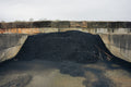 Heap of black material in a concrete container with a stone wall background