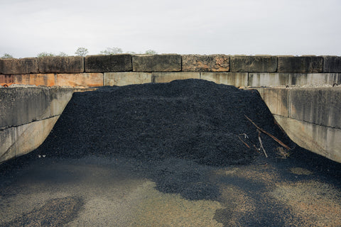Heap of black material in a concrete container with a stone wall background