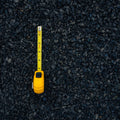 A yellow tape measure extended vertically over a dark gray and black gravel surface, showing measurement markings.