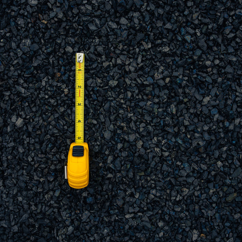A yellow tape measure extended vertically over a dark gray and black gravel surface, showing measurement markings.