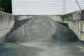 Pile of gravel or sand in a concrete basin with a white wall in the background