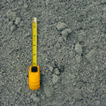 A yellow tape measure extended vertically over a textured gray gravel or concrete surface, showing the measurement scale.