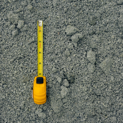 A yellow tape measure extended vertically over a textured gray gravel or concrete surface, showing the measurement scale.