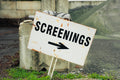 Rust-covered sign pointing to 'Screenings' with a black arrow on a concrete block.