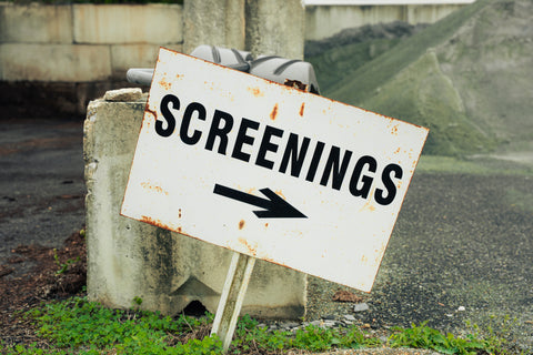 Rust-covered sign pointing to 'Screenings' with a black arrow on a concrete block.