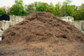 Large pile of compost or mulch with trees and concrete barriers in the background