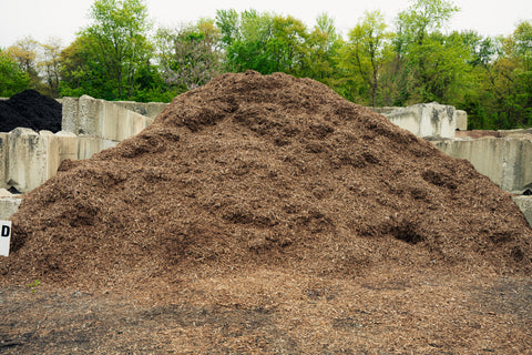 Large pile of compost or mulch with trees and concrete barriers in the background