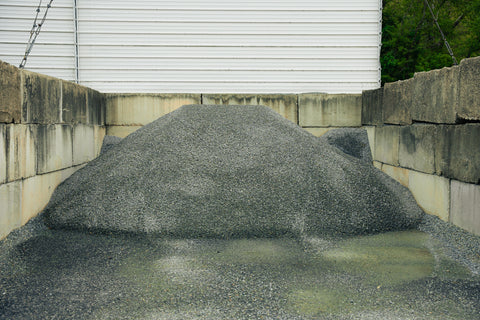 Large pile of gravel against a building with a concrete wall.