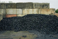 Heap of black gravel or coal in front of a stone wall.