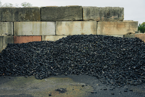 Heap of black gravel or coal in front of a stone wall.
