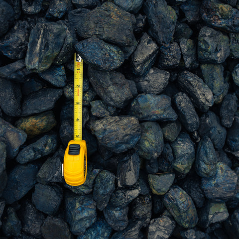 A yellow tape measure lies on top of a pile of dark, rough industrial rocks or coal blocks, showing its scale against the material.