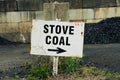 Rustic sign pointing to 'Stove Coal' with a brick wall and coal pile in the background.