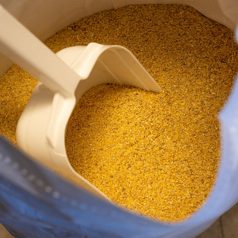 A 50 lb bag of The Mill Broiler Mash Chicken Feed with a scoop, showing poultry feed for broiler chickens.