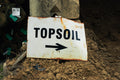 Sign pointing to topsoil with soil and containers in the background